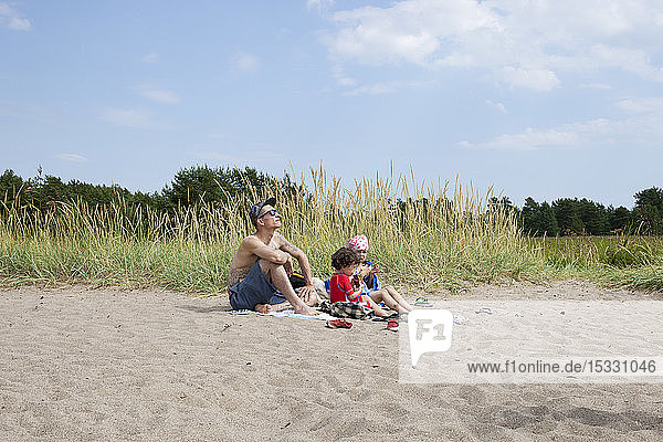 Mittlerer erwachsener Mann und Kinder sitzen am Strand