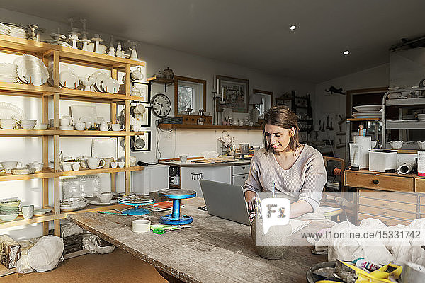 Woman using laptop in pottery workshop