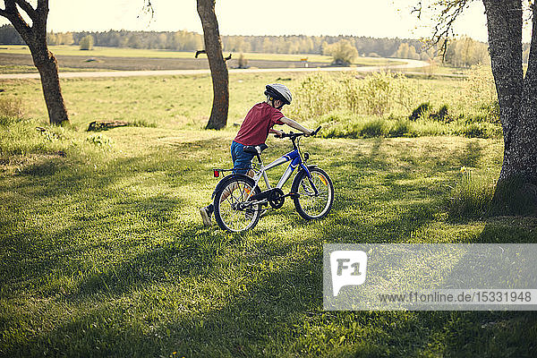 Boy pushing bicycle in on lawn
