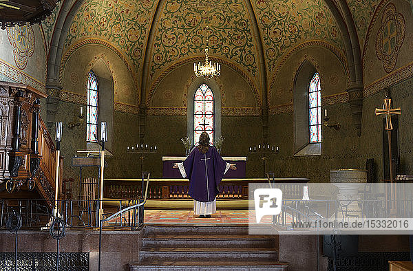 Priester in violettem Gewand am Altarraum einer Kirche stehend