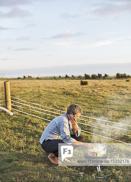 Woman talking on smart phone while cooking on grill
