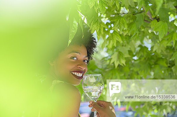 Lächelnde junge Frau mit einem Glas Weißwein unter einem Baum