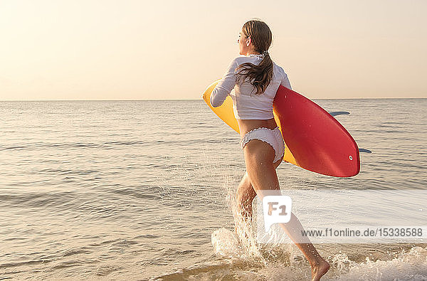 Woman holding surfboard running into sea