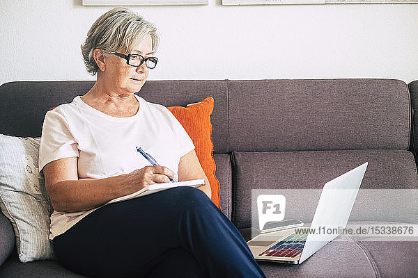 Senior woman holding pen using laptop on sofa