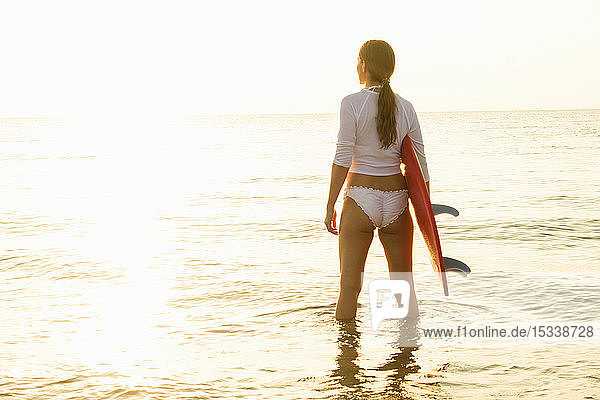 Frau hält Surfbrett im Meer bei Sonnenuntergang