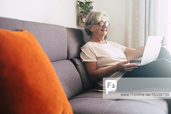 Lächelnde ältere Frau mit Laptop auf dem Sofa
