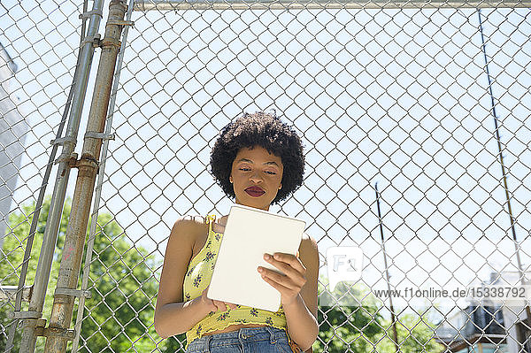 Young woman using digital tablet by wire fence
