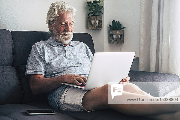 Älterer Mann mit Laptop auf dem Sofa