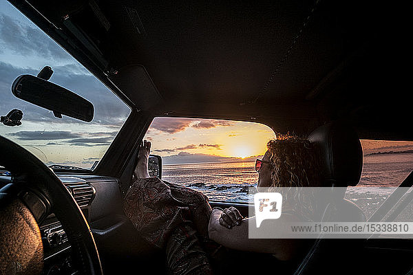 Frau im Auto mit angezogenen Beinen bei Sonnenuntergang