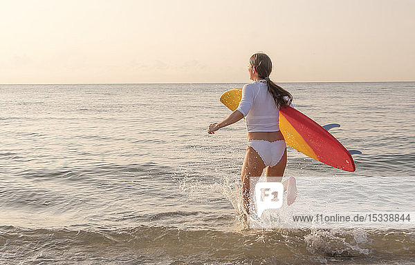 Frau hält Surfbrett und läuft ins Meer