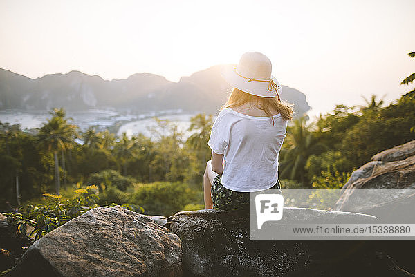 Frau mit Strohhut auf einem Felsen sitzend bei Sonnenuntergang auf den Phi Phi Inseln  Thailand
