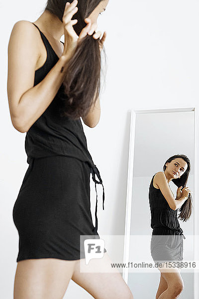 Woman wearing black dress with her hands in her hair by mirror