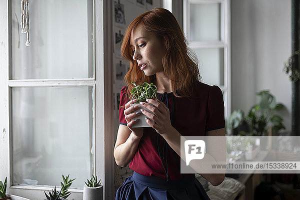 Rothaarige Frau hält Topfpflanze am Fenster
