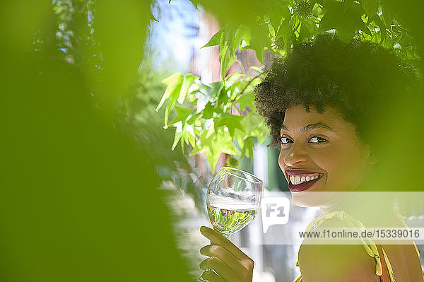 Lächelnde junge Frau mit einem Glas Weißwein unter einem Baum