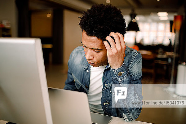 Besorgter männlicher Fachmann benutzt Laptop  während er am Bürotisch sitzt
