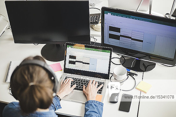 Schrägansicht einer Geschäftsfrau mit Laptop auf dem Schreibtisch  während sie im Kreativbüro sitzt
