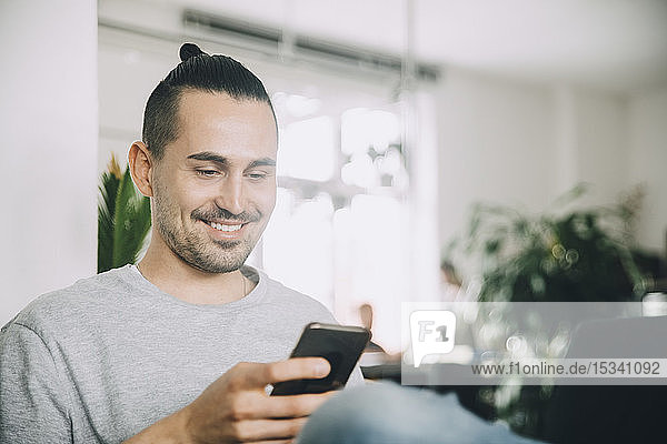 Kreativer Geschäftsmann lächelt  während er ein Smartphone im Büro benutzt