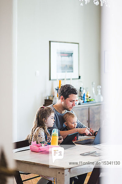 Father using laptop while sitting with cute children at table