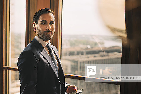 Portrait of confident male advisor standing by window at legal office