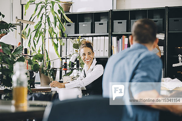 Lächelnde Geschäftsfrau schaut einen männlichen Kollegen an  während sie in einem kreativen Büro arbeitet