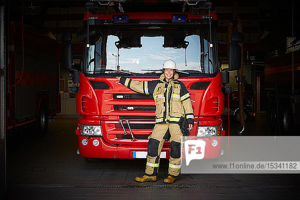 Full length portrait of smiling female firefighter standing in front of fire engine at fire station