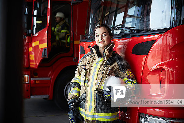 Porträt einer selbstbewussten Feuerwehrfrau  die in der Feuerwache am Löschfahrzeug steht