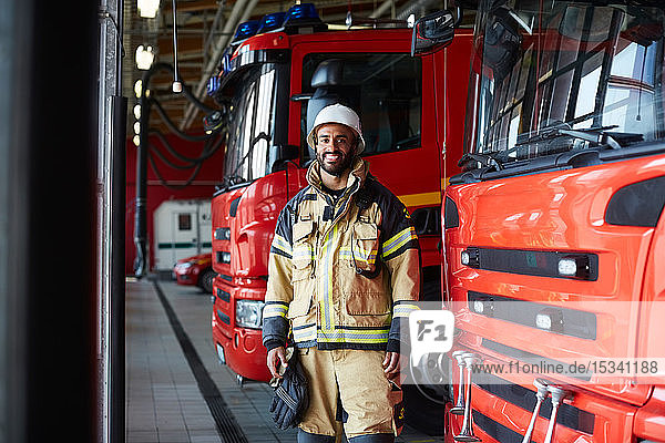 Portrait of smiling firefighter standing by fire engine at fire station