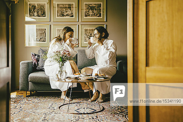 Couple in bathrobes drinking coffee while enjoying breakfast at hotel