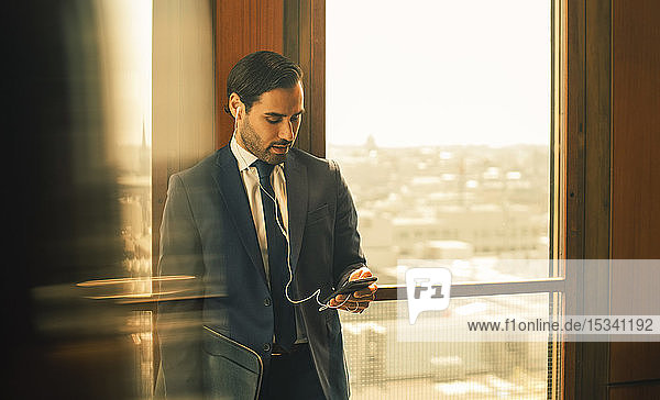 Mid adult legal professional using smart phone while standing against window at law office