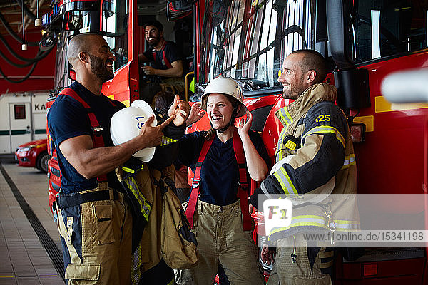 Fröhliche Feuerwehrleute diskutieren,  während sie in der Feuerwache beim Löschfahrzeug stehen