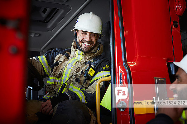 Smiling firefighter sitting in fire engine while talking to coworker