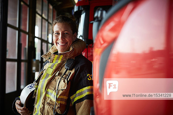 Porträt einer lächelnden Feuerwehrfrau  die in der Feuerwache beim Löschfahrzeug steht