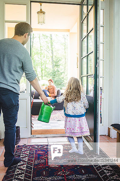 Father and daughter holding watering can while standing at home entrance