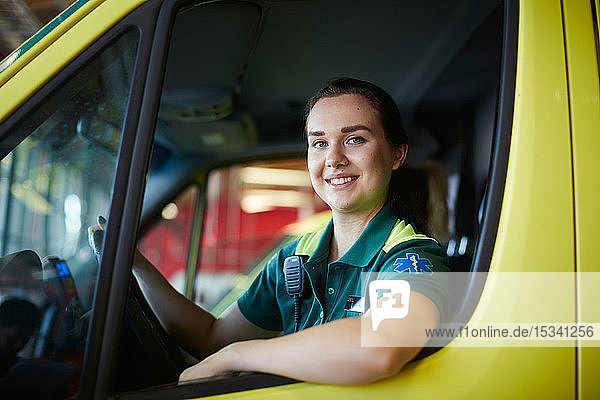 Porträt einer lächelnden jungen Sanitäterin  die einen Krankenwagen auf einem Parkplatz fährt