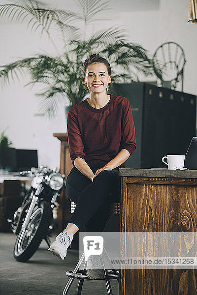 Porträt einer lächelnden kreativen Geschäftsfrau  die auf einer Kücheninsel im Büro sitzt