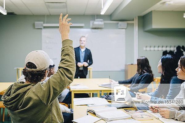 Teenager mit erhobener Hand während der Unterrichtsstunde im Klassenzimmer