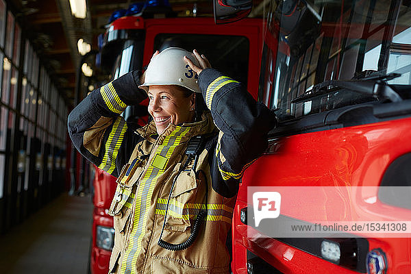 Smiling female firefighter wearing helmet while standing by fire engine at fire station