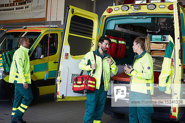 Männlicher Sanitäter spricht mit weiblicher Mitarbeiterin  während er auf dem Parkplatz beim Krankenwagen steht