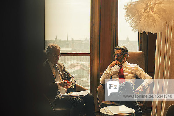 Male financial advisors discussing while sitting against window at law office