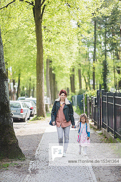 Mutter und Tochter halten sich beim Gehen auf dem Fußweg in voller Länge an den Händen