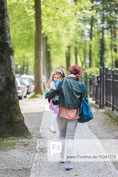 Rückansicht einer Mutter  die eine Tochter trägt  während sie auf einem Fußweg geht