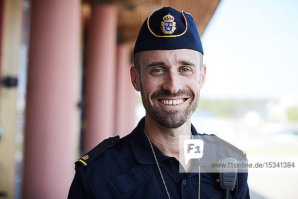 Porträt eines lächelnden Polizisten  der vor der Polizeistation steht