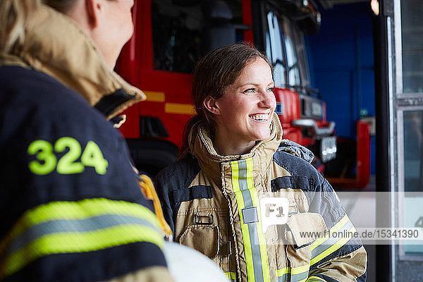 Smiling female firefighter standing with coworker in fire station