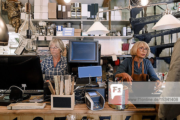 Leitende Verkäuferin im Gespräch mit einem männlichen Kunden  während ein Mitarbeiter den Computer an der Kasse im Laden benutzt