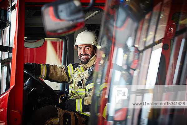 Portrait of mid adult firefighter sitting in fire truck at fire station