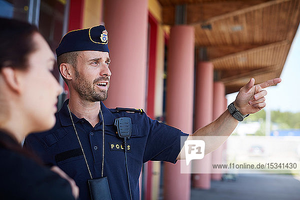 Männlicher Polizeibeamter zeigt auf einen Mitarbeiter vor einer Polizeistation  während er diesen anweist