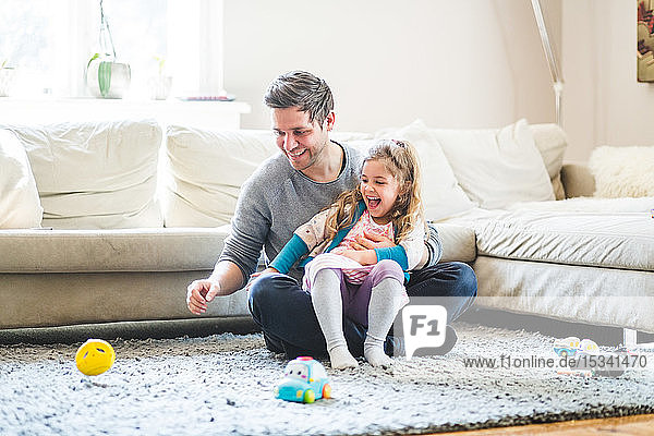 Cheerful father and daughter looking at toy while playing at home