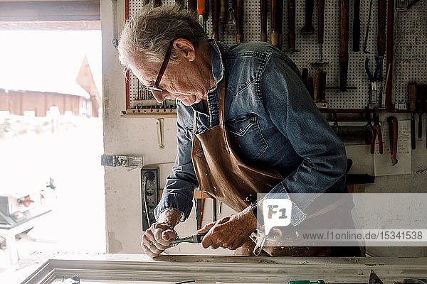 Senior male owner scraping window frame on workbench at store workshop