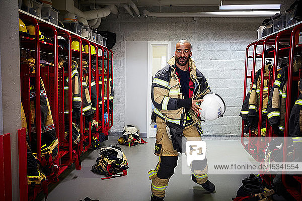 Male firefighter holding work helmet in locker room at fire station