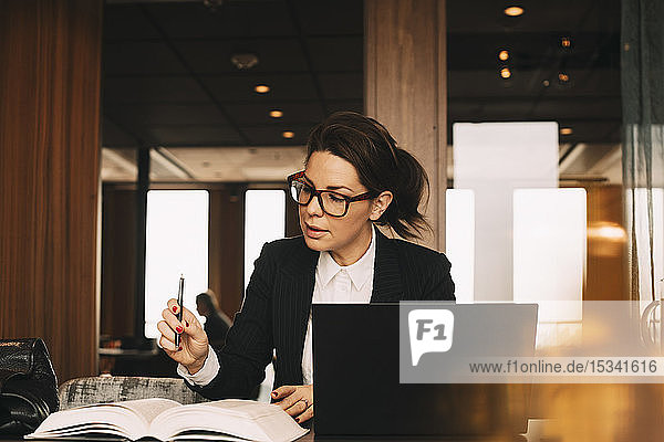 Female lawyer with laptop concentrating while reading book at office